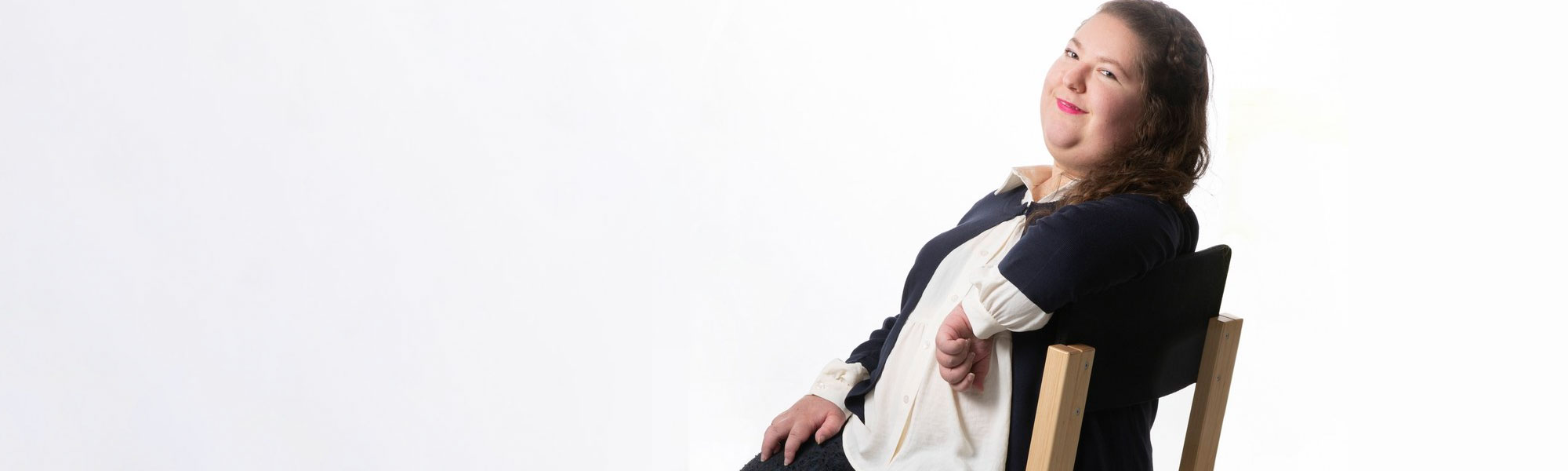 Selinä istuu tuolissa, käsi tuolin selkänojalla, ja hymyilee kameraan. Hänellä on mustavalkoiset vaatteet ja kirkkaan pinkki huulipuna. Tausta on valkoinen.